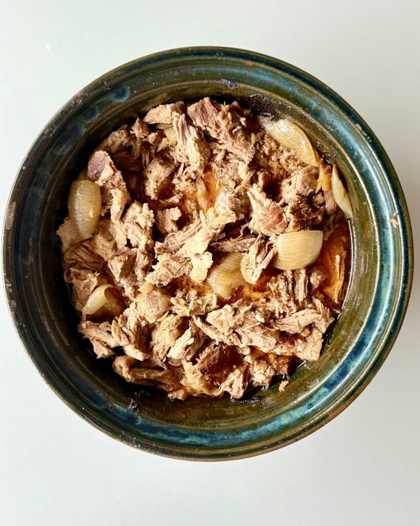 Sütőben sült, szaftos tépett tarja vöröshagymával, szójaszósszal és fűszerekkel, fehér tányéron tálalva