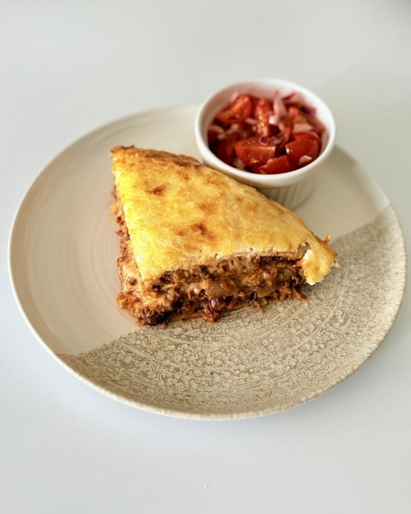 Rétegezett chilis bab torta teljes kiőrlésű tortilla lapokkal, darált marhahússal, vörösbabbal, tejföllel és olvadt sajttal sütve.