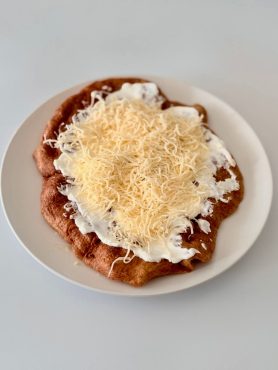 Aranybarnára sült teljes kiőrlésű lángos fokhagymás sajtos-tejfölös feltéttel, kívül ropogós, belül puha állaggal.