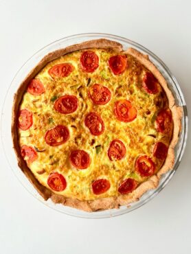 Teljes kiőrlésű tésztából készült paradicsomos-póréhagymás quiche aranybarnára sütve, paradicsommal a tetején.