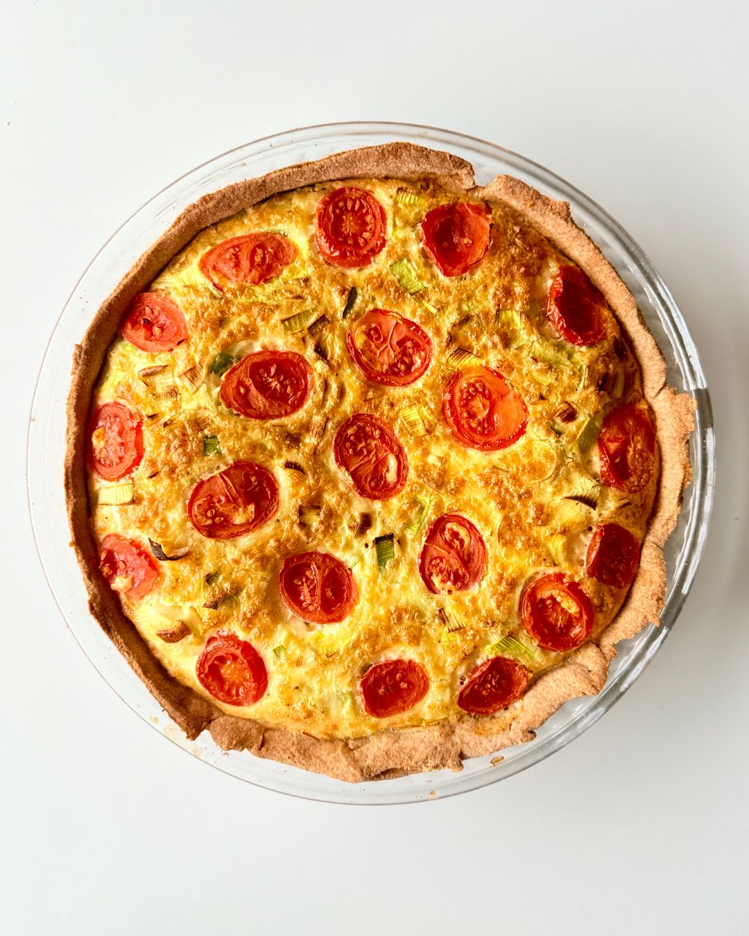 Teljes kiőrlésű tésztából készült paradicsomos-póréhagymás quiche aranybarnára sütve, paradicsommal a tetején.