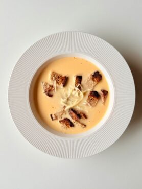 Krémes chilis sajtkrémleves pirított teljes kiőrlésű kenyérkockákkal és reszelt sajttal tálalva.