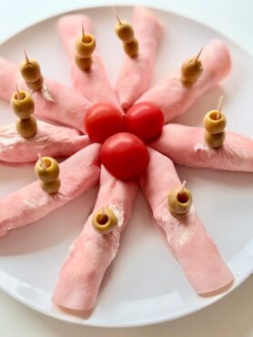 Túrókrémmel töltött sonkatekercsek koktélparadicsommal és zöld olajbogyóval díszítve, fogpiszkálóra tűzve.