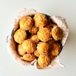 Frissen sült, teljes kiőrlésű túrós pogácsák ropogósra pirult sajtréteggel a tetejükön.