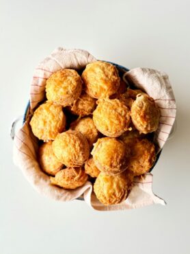 Frissen sült, teljes kiőrlésű túrós pogácsák ropogósra pirult sajtréteggel a tetejükön.