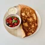 Ropogósra sült teljes kiőrlésű csirkés quesadilla fekete babbal, kukoricával és olvadt gouda sajttal, friss pico de gallóval tálalva.