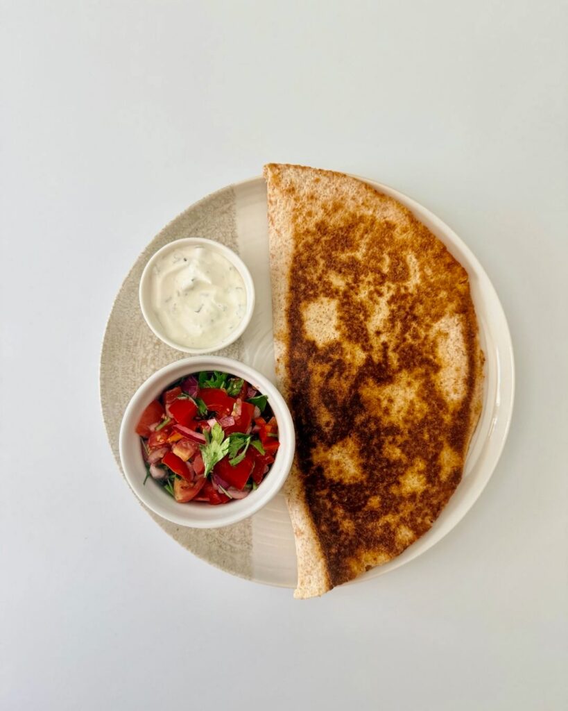Ropogósra sült teljes kiőrlésű csirkés quesadilla fekete babbal, kukoricával és olvadt gouda sajttal, friss pico de gallóval tálalva.